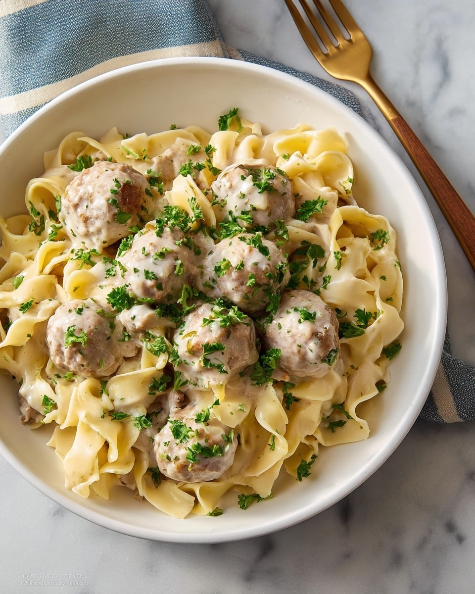Large white serving bowl filled with a generous portion of creamy meatball and egg noodle casserole, featuring perfectly round tender meatballs nestled among wide egg noodles coated in a rich, velvety cream sauce, sprinkled with fresh chopped parsley for a vibrant green contrast, photographed from a professional 3/4 angle view showcasing the entire dish in frame on a white marble countertop with natural lighting, styled like a hero shot from a food magazine, photo taken with an iphone --ar 4:5 --v 7