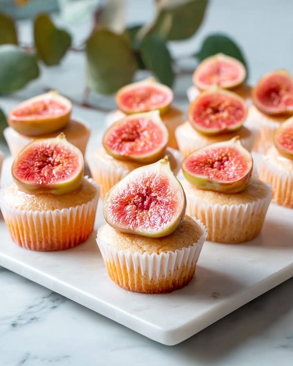White ceramic cupcake stand displaying a full batch of delicate yellow cupcakes each topped with a glossy slice of fresh fig, the cupcakes arranged neatly in white paper liners, surrounded by whole ripe figs on a white marble countertop, shot from a 3/4 angle with natural lighting, professional food magazine hero shot photo taken with an iphone --ar 4:5 --v 7