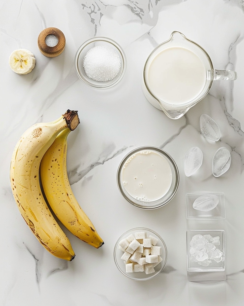 Single white glass filled with a creamy banana smoothie served over ice cubes, close-up angle showing the smooth texture and slight swirls of blended banana within the pale yellow drink, garnished subtly with a fresh banana slice on the rim, placed on a white marble surface in natural lighting, intimate plated serving photo taken with an iphone --ar 4:5 --v 7