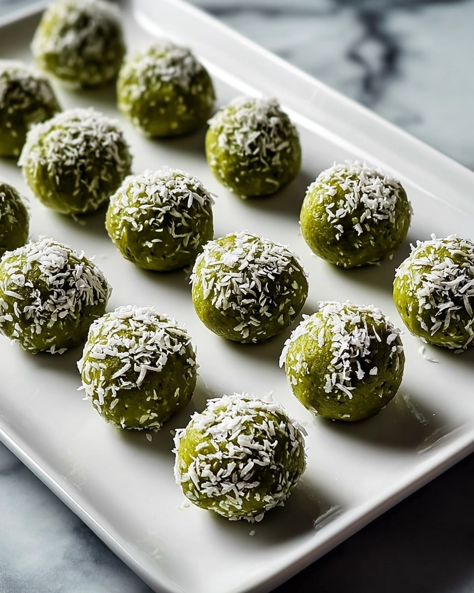 White rectangular platter filled with a full batch of green matcha energy balls, each generously coated on top with shredded coconut flakes, evenly arranged in neat rows, the whole dish presented with a clean, fresh look on a white marble countertop, captured with natural lighting from a 3/4 angle, professional food magazine hero shot photo taken with an iphone --ar 4:5 --v 7
