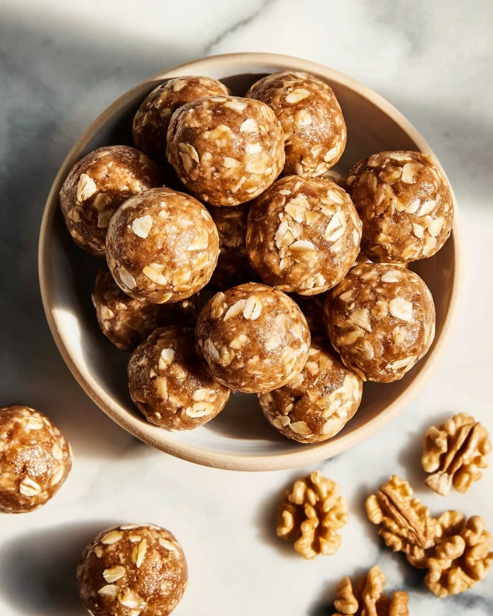 A large white bowl filled completely with a generous heap of round no-bake energy balls featuring visible oats embedded in a rich, caramel-colored base, accompanied by additional energy balls neatly arranged on a white marble countertop with whole walnuts scattered around, the entire scene captured in natural lighting with a professional food magazine styling, photo taken with an iphone --ar 4:5 --v 7