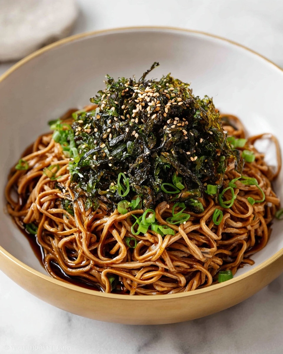 Large white bowl filled with a generous serving of glossy soba noodles mixed evenly with dark soy-based sauce, topped with a heaping mound of finely shredded, crisp roasted seaweed sprinkled with toasted sesame seeds and finely chopped green onions, whole dish photographed at a slight 3/4 angle on a white marble countertop with natural lighting, professional food magazine style photo taken with an iphone --ar 4:5 --v 7