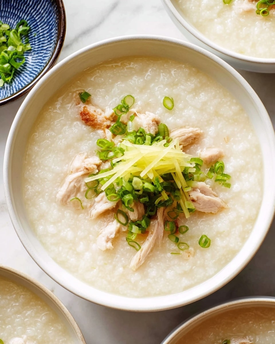 Large white bowl filled with steaming hot chicken congee, a creamy rice porridge with tender chicken pieces gently simmered within, garnished with a generous mound of julienned fresh ginger and vibrant chopped green onions on top, multiple matching white bowls arranged together displaying the comforting, hearty dish in a professional food magazine hero shot style on white marble countertop with natural lighting, photo taken with an iphone --ar 4:5 --v 7