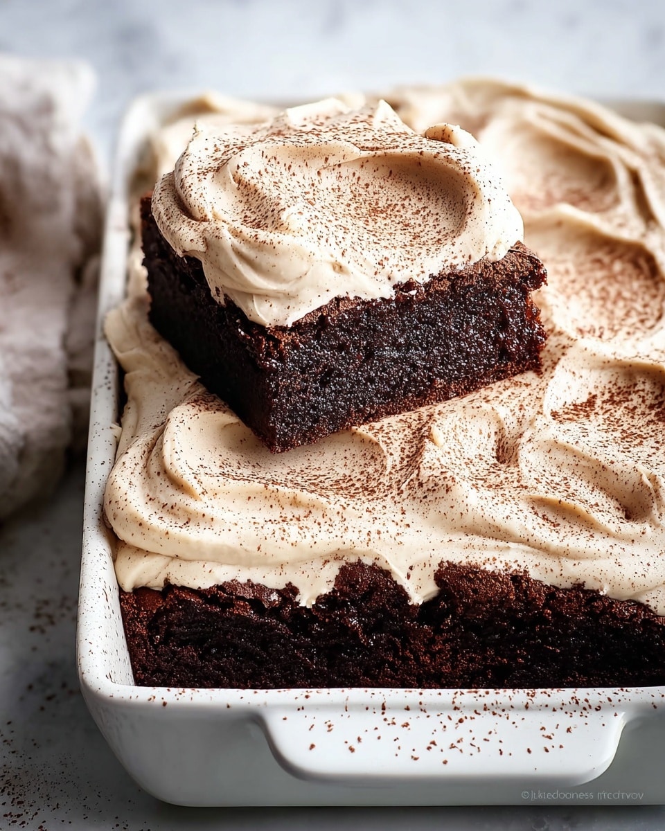 Full white rectangular baking dish filled with rich, dense chocolate brownies topped with an even layer of creamy, vanilla bean-speckled frosting, smooth and slightly rippled across the top, with a dusting of cocoa powder evenly spread over the surface, shot from a 3/4 angle on a white marble countertop with natural lighting, styled like a hero food magazine photo showing the entire uncut batch, photo taken with an iphone --ar 4:5 --v 7